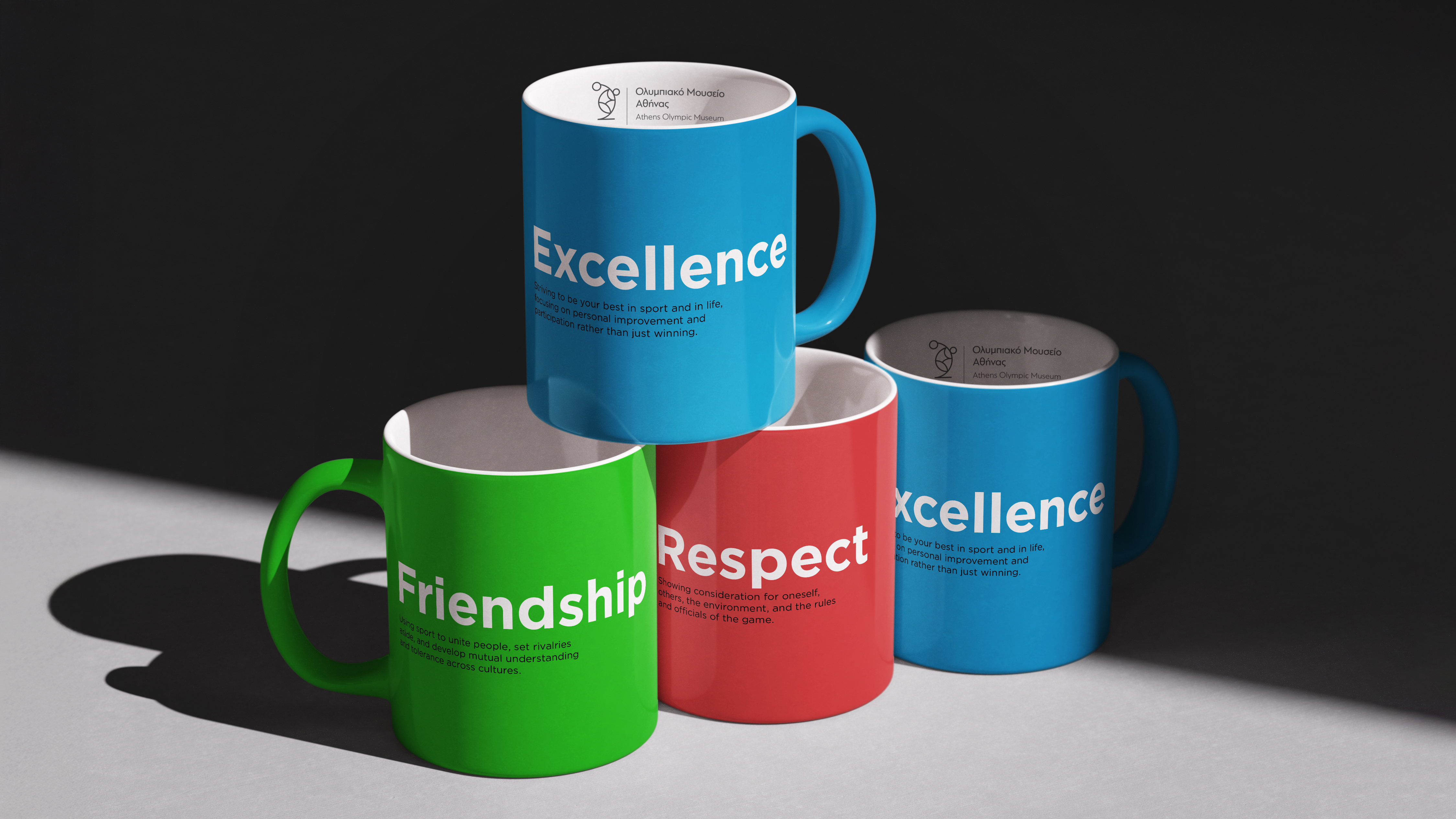 A stacked arrangement of three mugs in blue, green, and red, printed with the Olympic values 